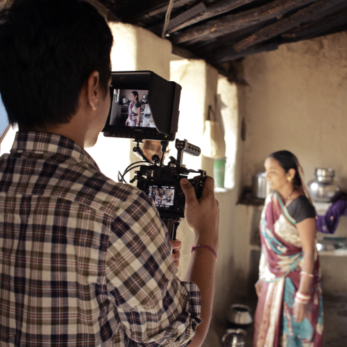 A camera man watches the display monitor on set while filming a woman in a traditional Indian garb.